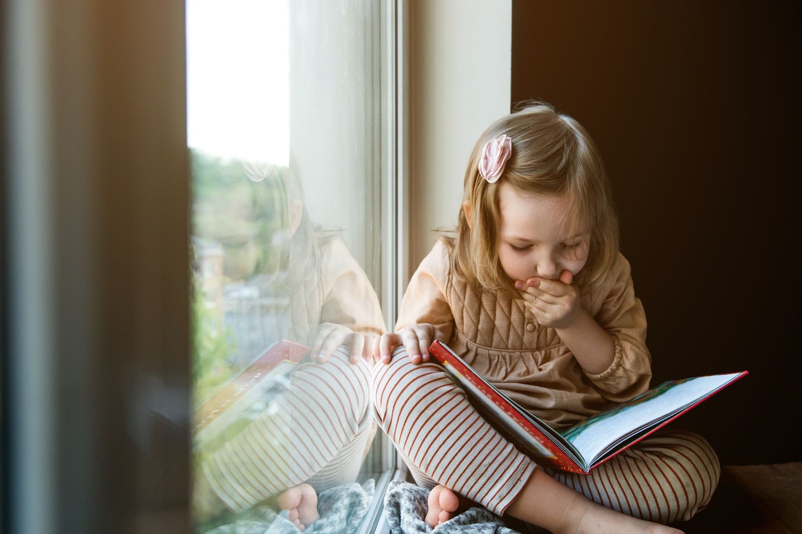Fetiță citește o carte stând jos.