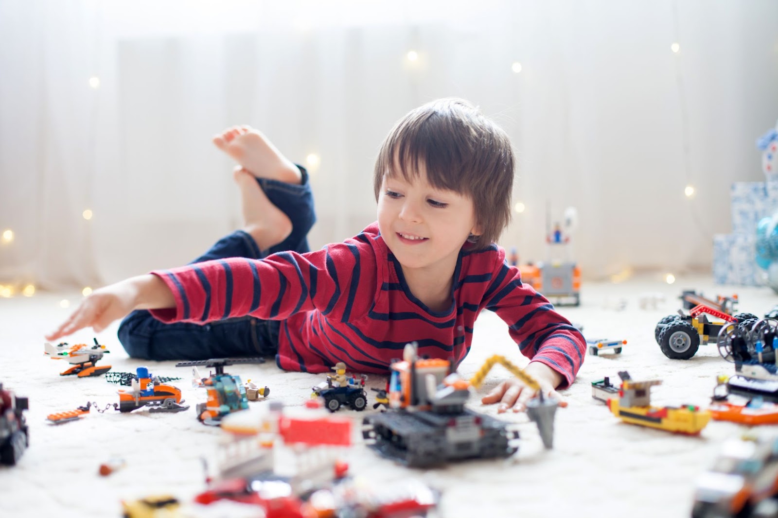 Băiețel se joacă pe podea cu piese lego colorate.